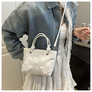 Detail of white lace bucket bag with butterfly embroidery and silver metal eyelets