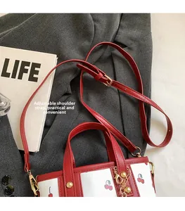 Detail of red cherry pattern tote bag with adjustable shoulder strap and gold hardware