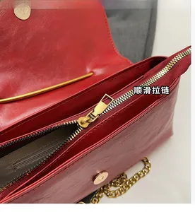 Detail of red leather crossbody bag showing the smooth zipper and golden metal chain