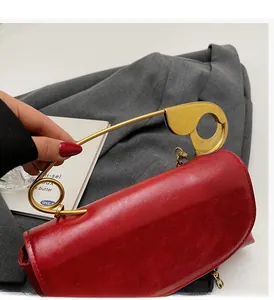 Detailed macro view of the red leather handbag with a gold safety pin shaped metal handle
