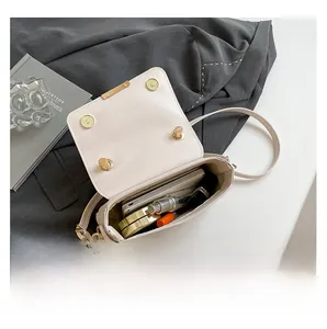 Interior capacity of the beige small square bag showing daily essentials and flap detail