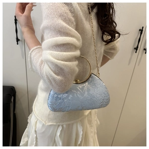 Detail of light blue crossbody box bag with gold ring handle and floral embroidery