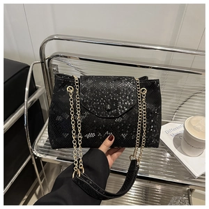 Detail of black python texture leather handbag with gold chain strap in modern setting