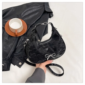 Detailed close-up of a black pleated crescent hobo bag featuring a silver bow accent