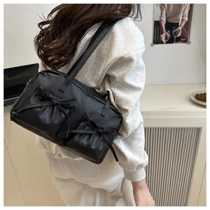 Detail of black faux leather shoulder bag with bow accents and side pockets