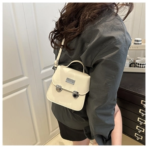 Vue latérale d'une femme portant un sac besace crème en cuir avec boucles argentées chez soi