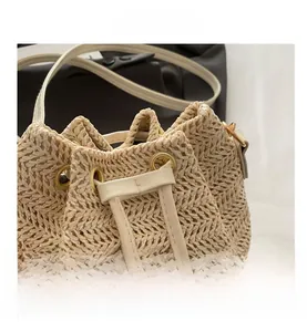 Detailed view of beige straw bucket bag featuring synthetic leather drawstring and metal eyelets