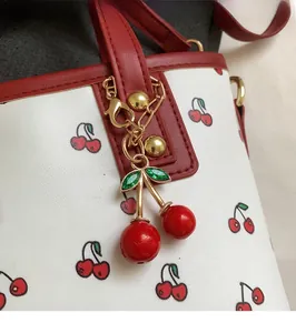 Detail of cute cherry charm on white leather tote with red cherry pattern print