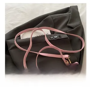 Close-up of pink leather handbag with gold buckle on gray blazer and white bedding