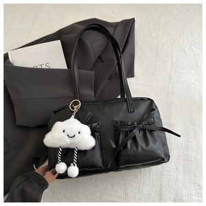 Detail of black tote bag with bow pocket and cute white cloud charm on white cloth