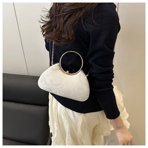 Detail of white evening box bag featuring intricate floral lace embroidery and gold ring handle