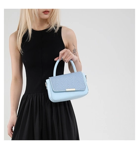 Détail du sac bandoulière bleu clair avec rabat tissé en V et finitions dorées