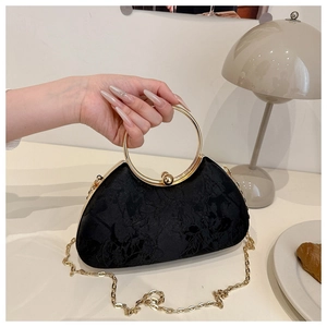 Detail of elegant black embroidered evening bag featuring a gold circular metal handle