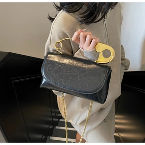 Detail of black glossy leather handbag with gold safety pin handle and chain strap