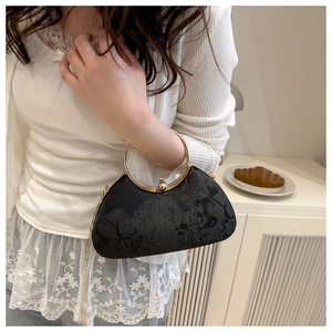 Detail of black embroidered handbag with gold ring handle and chain in a cafe setting