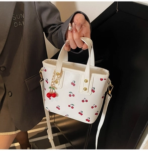 Detail view of white cherry print bucket bag with gold chain and 3D cherry pendant