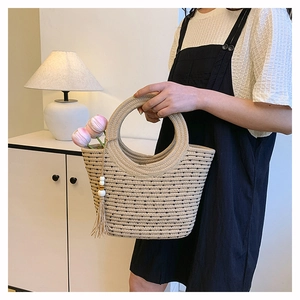 Detail view of woven straw tote bag with black polka dots, round handle and tassel charm