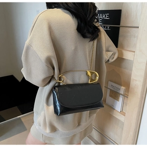 Detail of black crossbody bag featuring a unique oversized gold safety pin metal handle