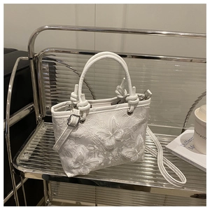 Dettaglio della borsa tote in pizzo bianco con ricamo a farfalla e chiusura in argento