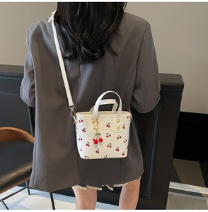Dettaglio di una borsa a secchiello bianca con stampe ciliegie e ciondolo 3D ciliegia