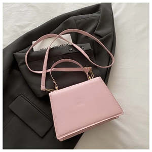 Pink leather trapezoid crossbody bag detail with top handle on a grey suit background