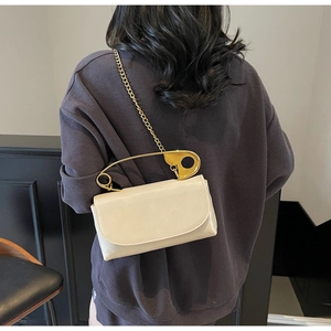 Detailed view of cream leather handbag with unique oversized gold safety pin handle