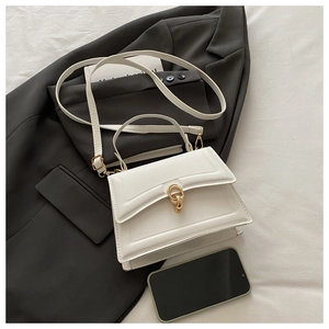 Detail view of white leather crossbody bag with gold double-ring buckle and strap