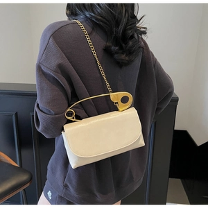Detail of off-white handbag with golden safety pin handle and fine gold chain strap