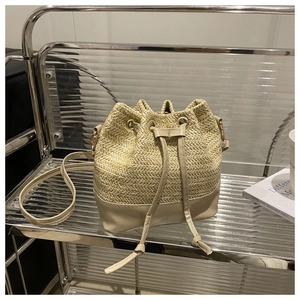 Detail of beige straw and cream leather bucket bag on an acrylic display stand