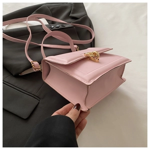 Detail of light pink square crossbody bag with gold metal twist lock on gray suit