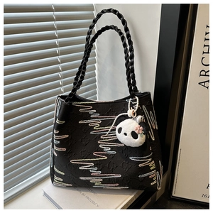 Detail of black tote bag with wave embroidery, woven handles and a panda plush charm