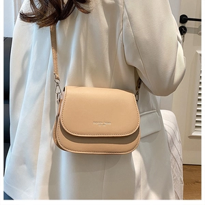 Side view of beige PU leather saddle bag with adjustable strap worn on a white suit