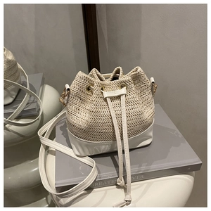 Detail view of woven straw and cream leather bucket bag with gold hardware drawstring closure