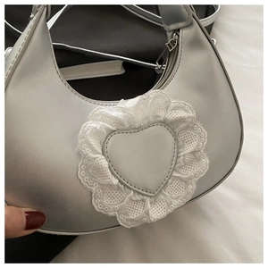 Detail of silver metallic crescent bag featuring heart patch and white lace trim