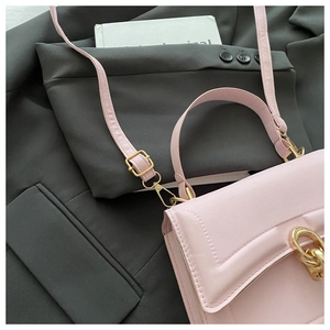 Close-up of pink crossbody bag with gold hardware and fine quilting on grey blazer