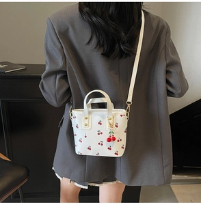 Detailed close-up of a white leather tote bag with cherry prints and a cute cherry charm