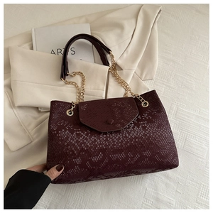 Détail d'un sac cabas bordeaux effet serpent avec chaîne dorée et finition cuir texturé