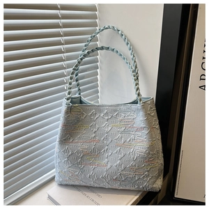 Detail of light blue tote bag featuring wavy colorful embroidery and braided rope handles