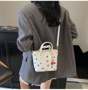 Rear view of a white mini bucket bag with red cherry print and a cherry chain charm