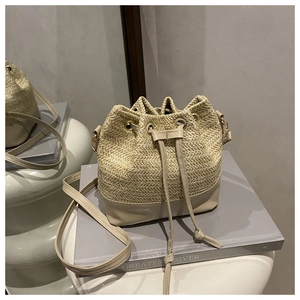 Close-up of cream woven straw bucket bag with leather拼接 details and drawstring close