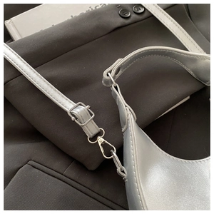 Detail of silver crescent shoulder bag featuring metallic finish and adjustable strap hooks