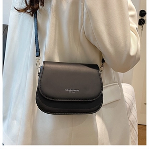 Detail of a minimalist black faux leather crossbody bag with silver fashion typography