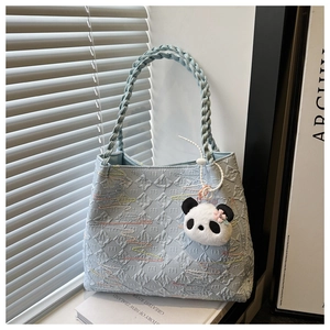 Detail of light blue quilted tote bag with chunky woven handle and panda plush charm