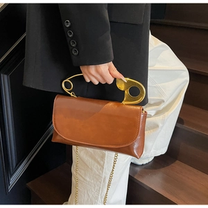Detail of creative brown crossbody bag with large gold safety pin handle and chain strap
