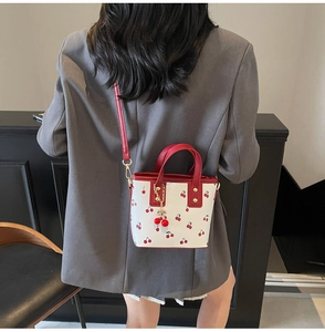 Detail of white PU bucket bag with cherry print and decorative cherry pendant on shoulder