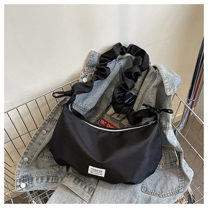 Détail du sac croissant noir avec bandoulière à volants et étiquette mode sur nylon