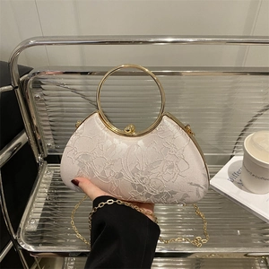 Elegant pink embroidered handbag with round metal handle and gold chain strap in a lifestyle setting