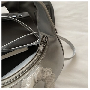 Close-up of silver crescent bag featuring delicate lace trim and metallic zipper detail