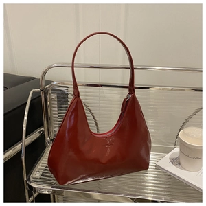 Detail view of a glossy dark red hobo bag on a glass shelf with books and a coffee cup