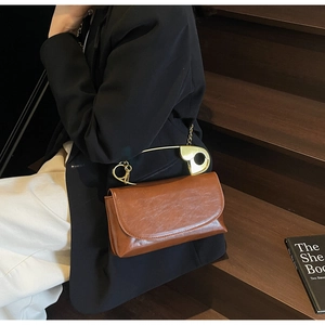 Close-up of brown vintage leather bag with unique gold safety pin handle and chain strap